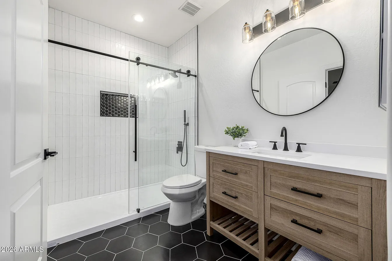 Bathroom with dark hex tile floor, round mirror, and glass shower door