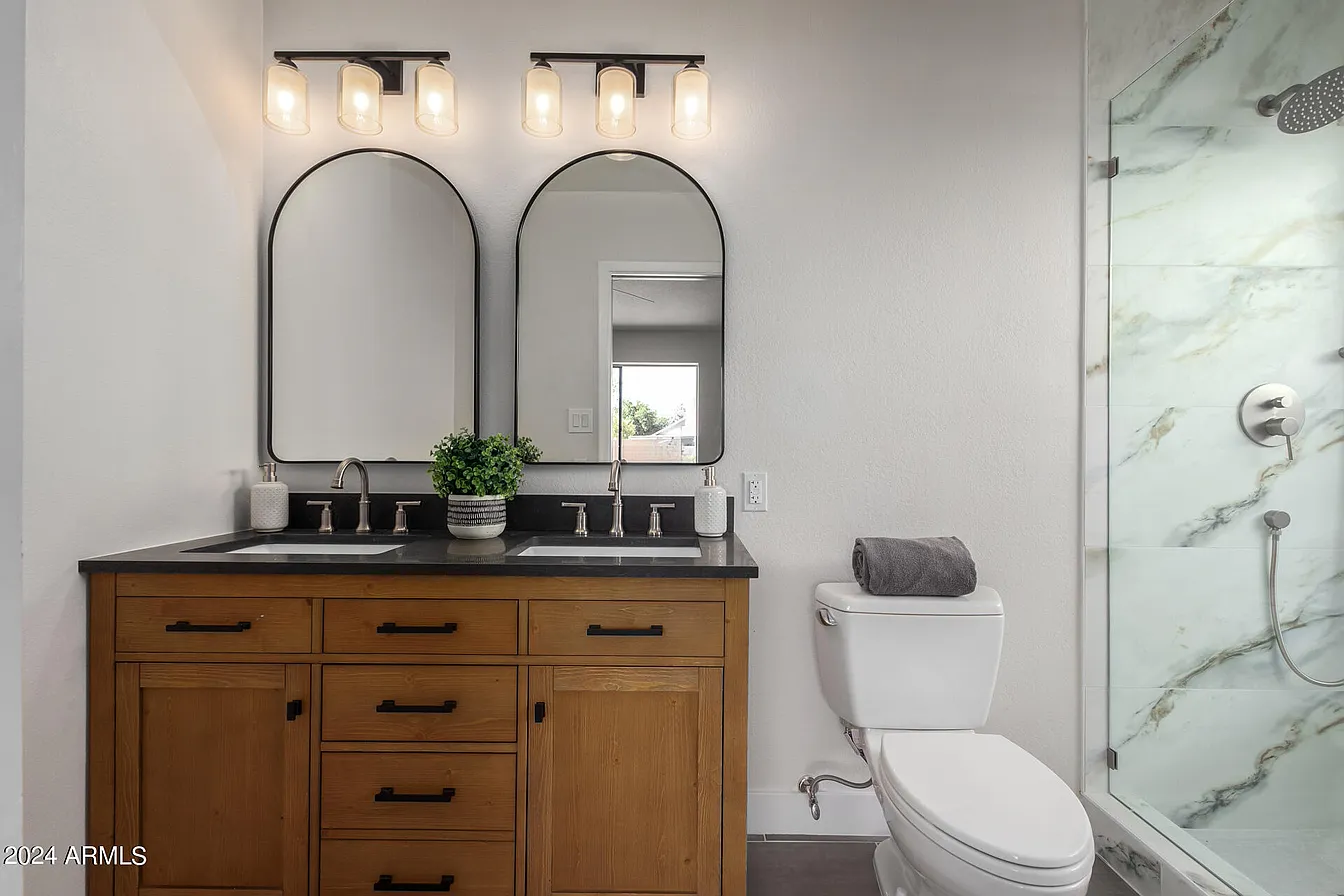 Bathroom with arched mirrors, wood vanity, and marble shower surround
